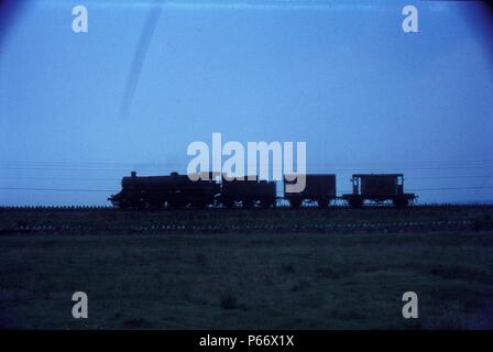 Un BR Standard Classe 4, 4-6-0 si avvicina a Carnforth con un prelevamento di merci dalla linea di Barrow. Foto Stock