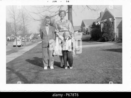 Fotografia in bianco e nero, mostrando una a pelo corto donna, che indossa un mantello, camicetta, e guanti, posa con due giovani ragazzi, sia indossando abiti, quello più piccolo che indossa un due-tonica camicia, con alberi, auto d'epoca, e case suburbane visibile in background, probabilmente fotografato in Ohio, Giugno 1956. () Foto Stock