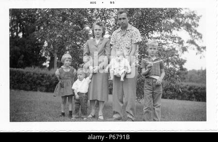 Fotografia in bianco e nero, mostrando una grande famiglia al di fuori di una impostazione erbosa, compreso un uomo che indossa una camicia con motivi floreali e pantaloni e una donna con capelli corti, indossando una gonna abito, circondato da quattro bambini bionda, ciascuno indossando un espressione seria, probabilmente fotografato in Ohio, Agosto 1955. () Foto Stock