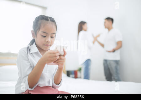 Bambina guarda al telefono mentre genitore litigi in camera da letto, foto design per problemi familiari e infelice nozione Foto Stock