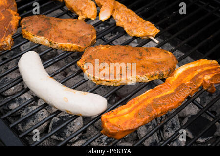 Grigliare salsicce e bistecche di carne fresca su barbecue grill. Foto Stock