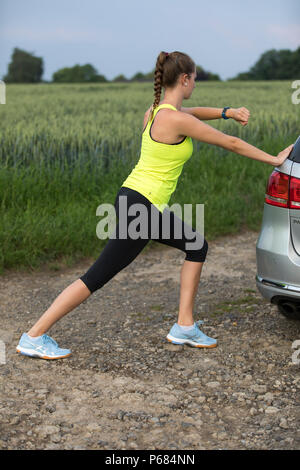 Giovane donna facendo esercizi di stretching, dopo una lunga corsa, jogging, guardando i valori del corpo su un orologio fitness, fitness tracker, sul, frequenza cardiaca, numero Foto Stock