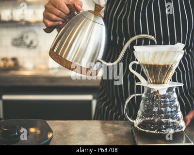 Barista infuso di caffè di gocciolamento, mano versando acqua calda dal bollitore sopra la polvere di caffè. Foto Stock