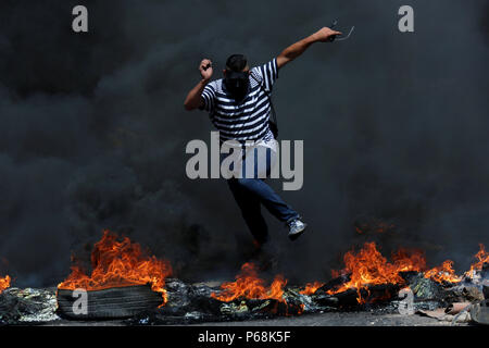 Ramallah, West Bank, Territorio palestinese. Il 29 giugno, 2018. Una mascherata manifestante palestinese salta in alto bruciando pneumatici durante gli scontri con le truppe israeliane a seguito di una dimostrazione vicino l'insediamento ebraico di Beit El, vicino a Ramallah in Cisgiordania occupata Giugno 29, 2018 Credit: Shadi Hatem APA/images/ZUMA filo/Alamy Live News Foto Stock