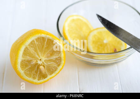 Un limone tagliato e due fette di limone nella lastra di vetro.parte della lama del coltello sulla lastra di vetro. Bianco sullo sfondo di legno. Foto Stock