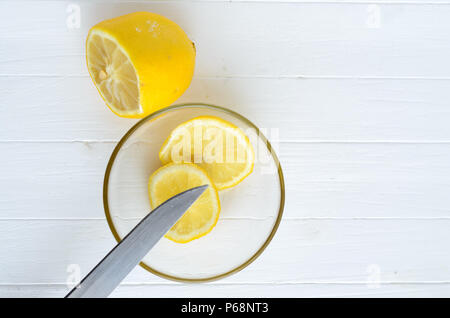 Un limone tagliato e due fette di limone nella lastra di vetro.Un limone è sulla parte superiore e due fette di limone nella lastra di vetro sono verso il basso.parte di coltello blad Foto Stock