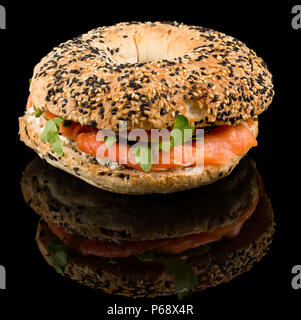 Bagel Salmone affumicato - sfornato fresco bagel, crema di formaggio e rabboccato con salmone affumicato e cipolle rosse con la riflessione isolata su sfondo nero Foto Stock