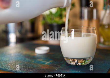 Mano fresco versatore kefir probiotik bere dalla bottiglia bianca in vetro chiaro sul tavolo da cucina. Foto Stock