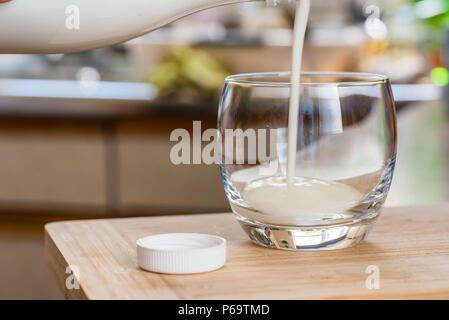 Mano fresco versatore kefir probiotik bere dalla bottiglia bianca in vetro chiaro sul tavolo da cucina. Foto Stock