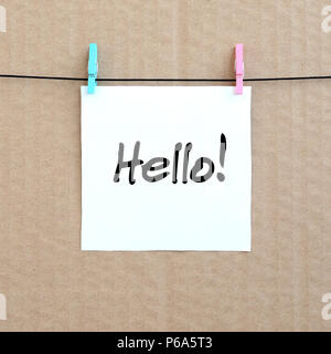 Ciao! Nota è scritta su un adesivo bianco che si blocca con un clothespin su una fune su uno sfondo di cartone marrone . Foto Stock