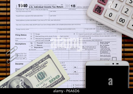 Composizione di elementi giacenti sul 1040 forma fiscale. Le fatture del dollaro, calcolatrice, smartphone, la graffetta e il blocco note. Il tempo a disposizione per pagare le tasse . Foto Stock