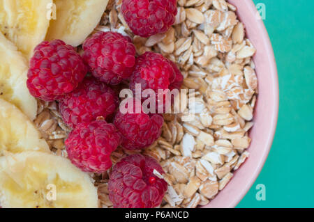 Close up di farina di avena in un bel rosa ciotola con fresche dolci rasberry e fette di banana su sfondo turchese. Foto Stock