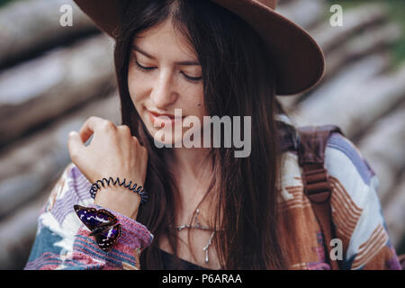 Felice elegante ragazza di viaggiatori in hat holding splendida farfalla colorata a mano. hipster donna che viaggia e esplorare. spazio per il testo ambientali Foto Stock