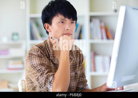 Giovane uomo utilizzando computer, guardando il pensiero del computer Foto Stock
