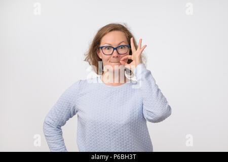 Giovane donna europea closinge la sua bocca come sulla cerniera lampo su sfondo grigio. È lei che mostra che può mantenere segreto. Foto Stock