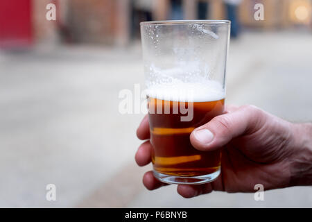 Un maschio di mano che tiene una pinta di botte ale / la birra artigianale Foto Stock