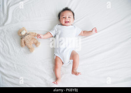 Ritratto di un bambino gattona sul letto in camera sua, adorabile baby boy in bianco e luminosa camera da letto, neonato relax nel letto, vivaio di giovani bambini Foto Stock