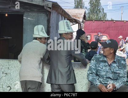 Gli uomini del Kirghizistan con kalpak cappelli a domenica il mercato degli animali, Karakol, Kirghizistan Foto Stock