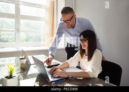 Giovani happy businessman mostrando qualcosa per il suo partner sul computer portatile in ufficio Foto Stock
