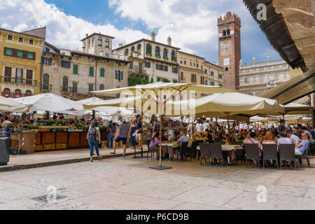 Verona, Italia piazza delle Erbe edifici tradizionali. Folla di mangiare accanto all aria aperta le bancarelle del mercato sulla piazza del mercato di ristoranti. Foto Stock