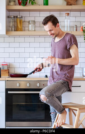 Foto di brunet uomo con padella e telefono nelle sue mani in cucina Foto Stock