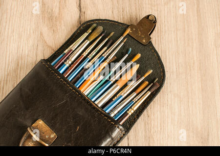 Aprire vintage custodia in pelle scatola piena di diversi tipi di vernice usata spazzole sulla superficie di legno sfondo Foto Stock
