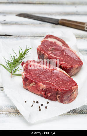 Secco nervatura di età-eye steak crudo su carta e lo sfondo di legno. Foto Stock