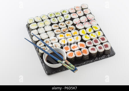 Set di maki sushi sulla scheda di ardesia con salsa di soia e bastoncini isolato su bianco. Foto Stock