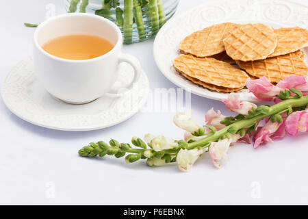 Tazza di tè, biscotti e fiore su sfondo bianco Foto Stock