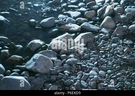 Acqua liscia indossato sassi o pietre di forma irregolare e di dimensioni in un alveo fluviale in un frame completo texture di sfondo Foto Stock