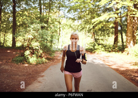 Montare la giovane donna in abbigliamento sportivo di ascoltare la musica in cuffia mentre è in esecuzione solo su di un percorso attraverso una foresta Foto Stock