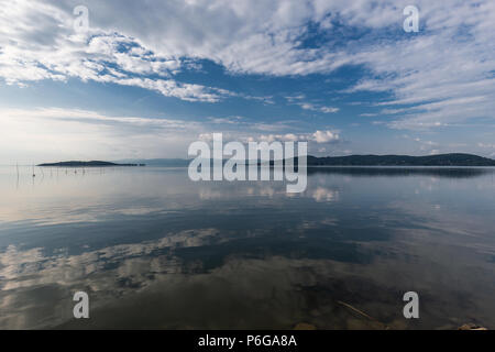 Perfettamente simmetrica vista del lago Trasimeno (Umbria, Italia) con nuvole, cielo e isole riflettendo sull'acqua Foto Stock