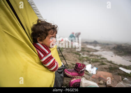 Un giovane bambino guarda fuori da una tenda al campo di fortuna della frontiera Greek-Macedonian vicino al villaggio greco di Idomeni. Foto Stock