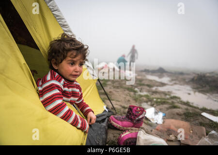 Un giovane bambino guarda fuori da una tenda al campo di fortuna della frontiera Greek-Macedonian vicino al villaggio greco di Idomeni. Foto Stock