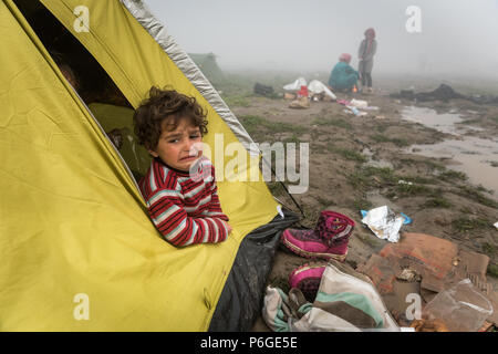 Un giovane bambino guarda fuori da una tenda al campo di fortuna della frontiera Greek-Macedonian vicino al villaggio greco di Idomeni. Foto Stock