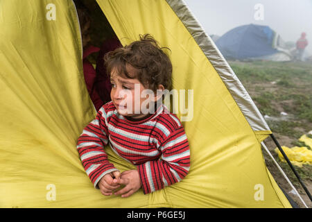 Un giovane bambino guarda fuori da una tenda al campo di fortuna della frontiera Greek-Macedonian vicino al villaggio greco di Idomeni. Foto Stock