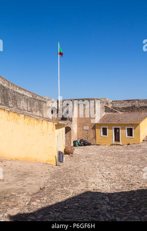 La piazza d'ingresso lastricata da ciottoli, dell'area del castello di Castro Marim, Algarve, Portogallo. Facciata gialla degli edifici. Mura di fortificazione w Foto Stock