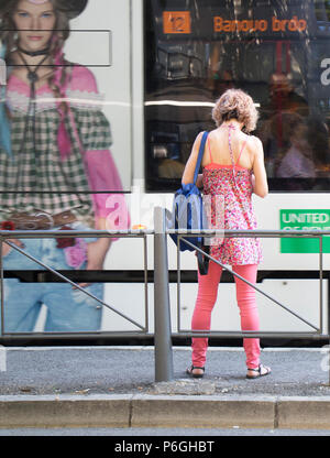 A Belgrado, in Serbia - Giugno 1, 2018 : Una bionda donne nel casual outfit rosa in piedi ad una fermata di autobus e di attesa per i mezzi di trasporto pubblico su un soleggiato molla Foto Stock