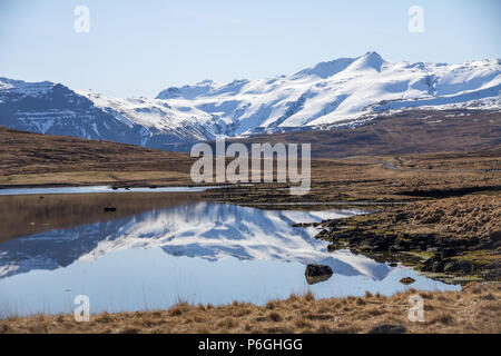 Montagne coperte di neve in Islanda della penisola Snaefellsness sono riflesse nel piccolo lago. Un tratto di strada tranquilla passa attraverso il paesaggio Foto Stock