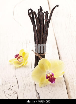 La vaniglia essiccata frutti e orchidee vaniglia fiori bianco sullo sfondo di legno. Foto Stock