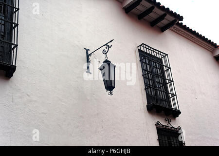 Un muro bianco a Bogotà con appesi via la luce e un sacco di sicurezza sotto forma di barre decorative su windows. Foto Stock