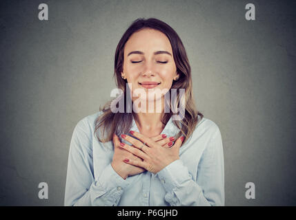 Donna con gli occhi chiusi tiene le mani sul petto vicino al cuore, mostra la gentilezza, esprime sincere emozioni, essendo natura generosa. Il linguaggio del corpo sentimenti concept Foto Stock