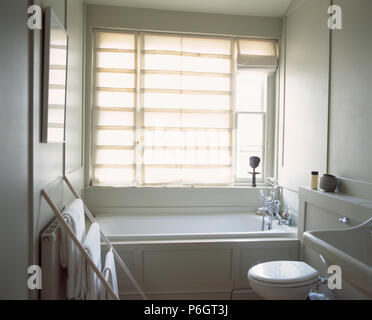 Biancheria da letto bianca Roman cieco sulla finestra sopra bagno in piccole stanze da bagno di colore bianco con asciugamani bianchi su semplici rack in legno Foto Stock