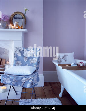 Blue+white floral loose-coperchio sulla sedia accanto a roll-top bagno in blu pallido bagno Foto Stock