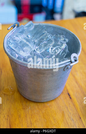 La benna di argento del cubo di ghiaccio sul tavolo di legno con uno sfondo di goccioline di acqua Foto Stock