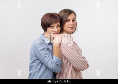 Bella maturesenior mamma e sua figlia adulta sono abbracciava, guardando la fotocamera e sorridente. Foto Stock