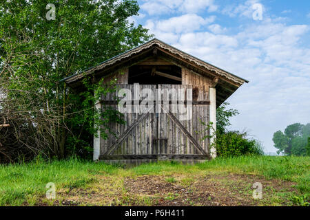 Il vecchio fienile con le nuvole ed erba nella foresta bavarese e un campo di fronte Foto Stock