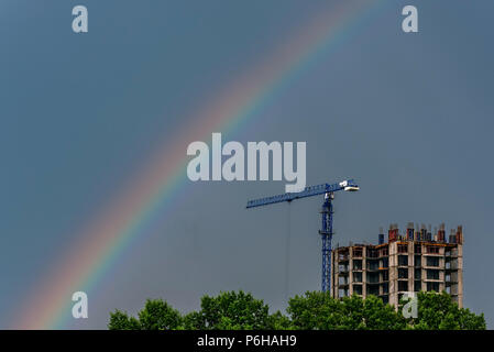 Bellissimo arcobaleno sopra gli alberi, la costruzione di un edificio alto e una gru contro il cielo blu Foto Stock