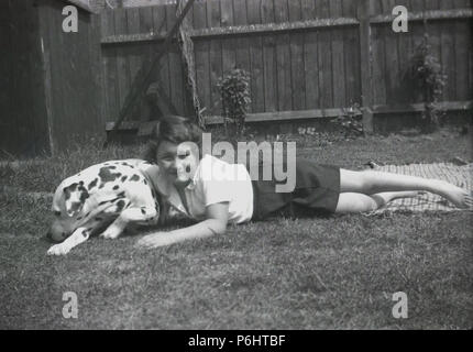 Degli anni Cinquanta, giovani schoolgirl disteso al di fuori in un giardino su un tappeto con il suo animale domestico cane dalmata. Un unqiue razza pezzata, Dalamations sono buona famiglia cani, cortese, intelligente e giocoso. Foto Stock