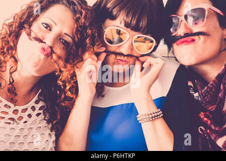 Tre femmine caucasica amici stare insieme in amicizia e follia usando i capelli come baffi e felicità il concetto di relazione. vintage c pieno Foto Stock